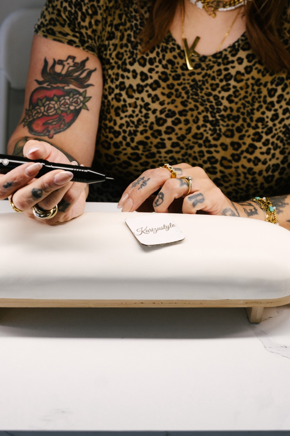 Karina at her jewelry bench in leopard print, holding her pen beside a Karizustyle tag